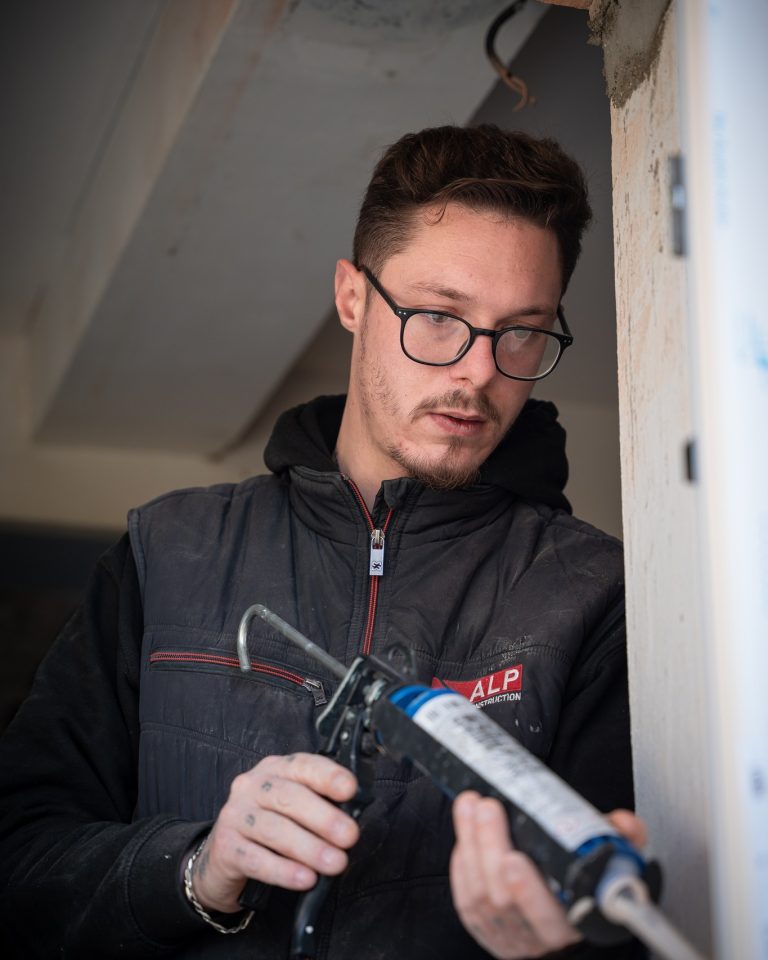 Un salari&eacute; ALP, v&ecirc;tu d&rsquo;une veste au logo de l&rsquo;entreprise, pr&eacute;pare une menuiserie.