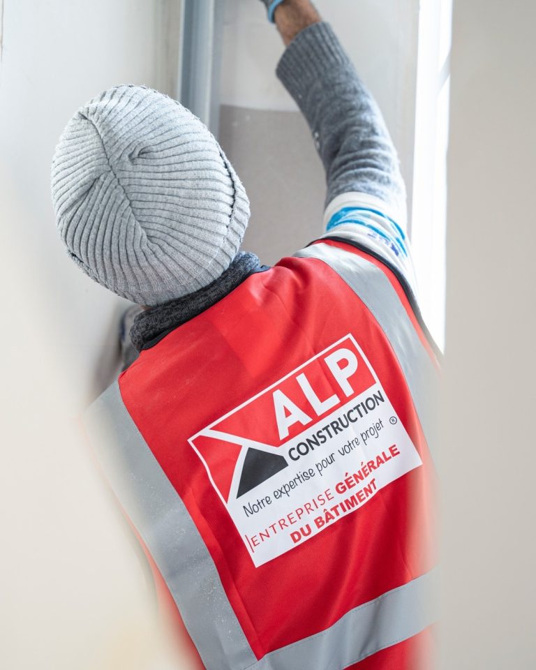 Un salari&eacute; pr&eacute;pare un mur int&eacute;rieur, avec le logo ALP visible dans le dos de son gilet.
