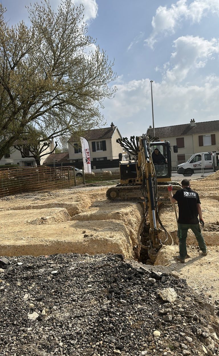 Un salari&eacute; portant le logo ALP travaille &agrave; c&ocirc;t&eacute; d&rsquo;une pelle m&eacute;canique sur un chantier de terrassement.