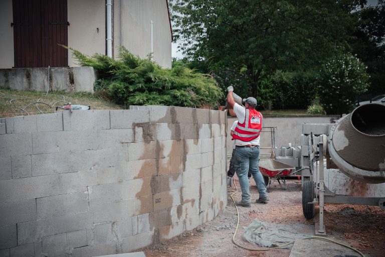 Un salari&eacute; ALP vu de dos r&eacute;alise les finitions d&rsquo;un mur ext&eacute;rieur pr&egrave;s d&rsquo;une b&eacute;tonni&egrave;re.
