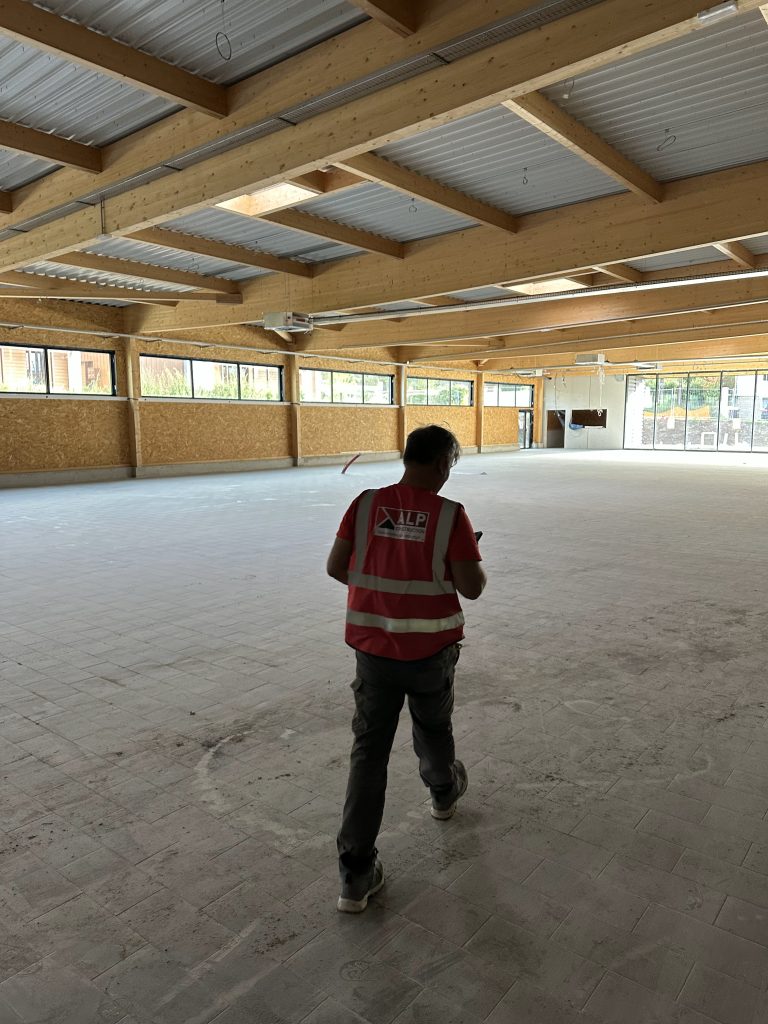 Un membre de l&rsquo;&eacute;quipe ALP, vu de dos en gilet rouge, parcourt un b&acirc;timent en travaux.