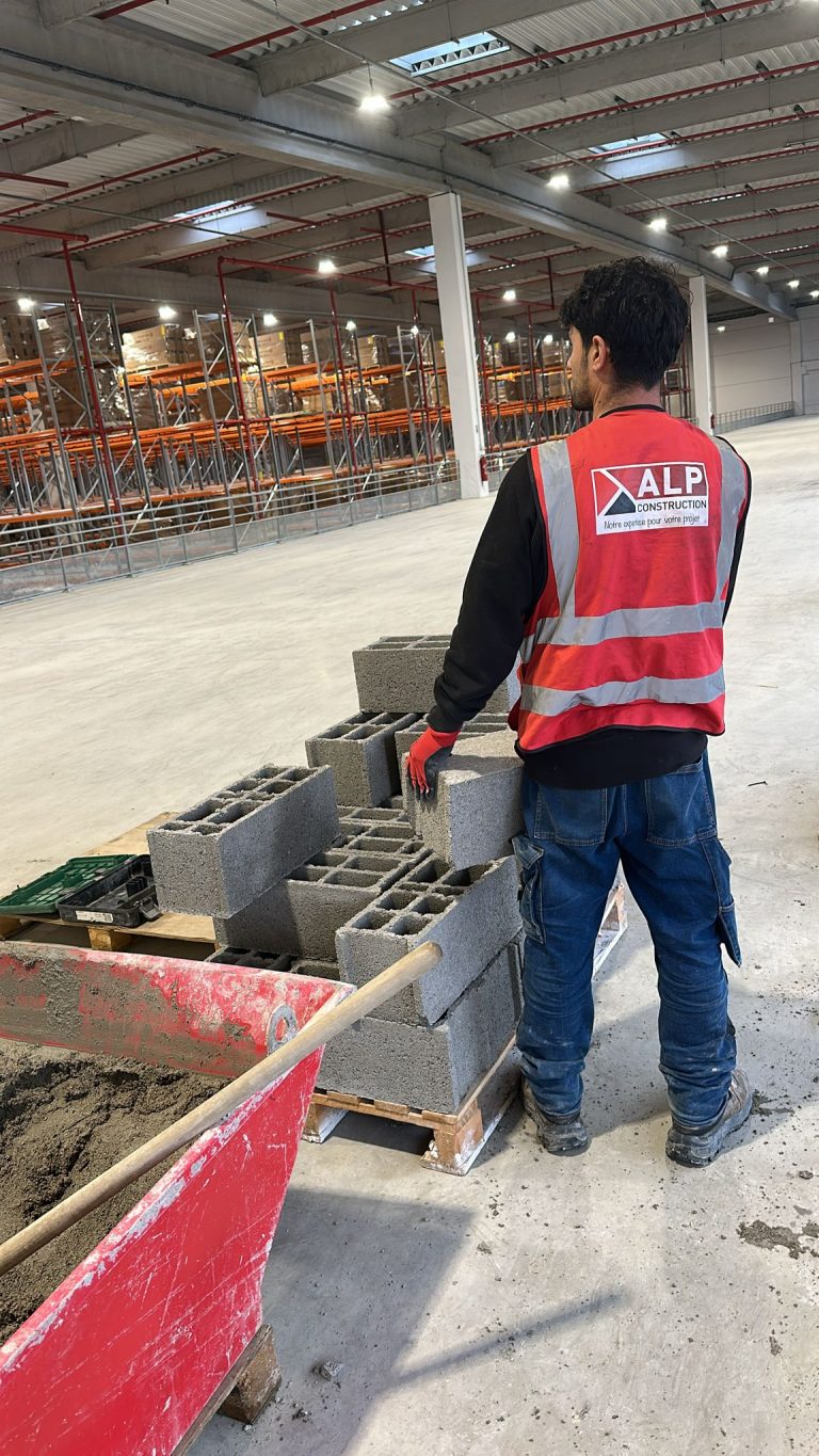 Un salarié ALP vu de dos prépare les blocs pour un muret intérieur.