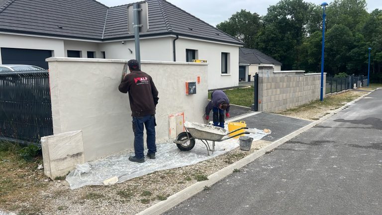 Deux salariés interviennent sur un mur de clôture, avec le logo ALP visible au dos d’une veste.