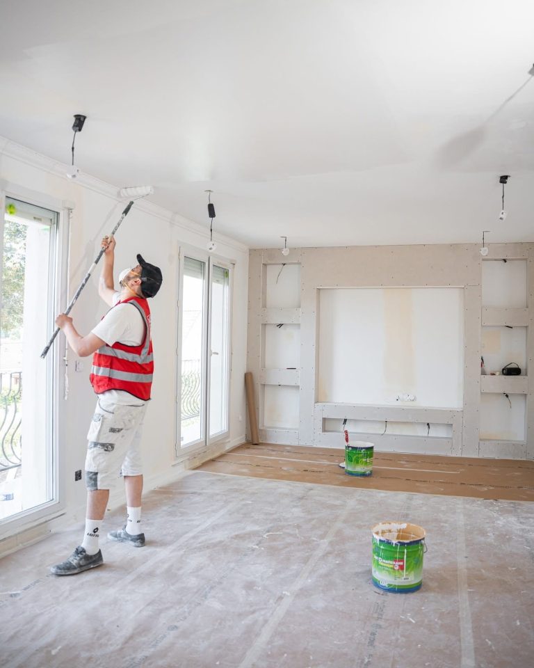 Un peintre ALP applique la peinture au rouleau sur un plafond intérieur.